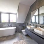 Modernes Badezimmer mit freistehender Badewanne, Doppelwaschbecken und grauen Fliesen. Favorent Ferienimmobilien Management.