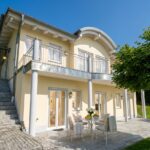 Helles Ferienhaus mit Terrasse und Gartenmöbeln unter blauem Himmel. Favorent bietet professionelle Ferienhausverwaltung.