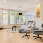 Wohnzimmer mit Sofa, Sessel und Blick aus dem Fenster, geeignet für die Ferienhausverwaltung.