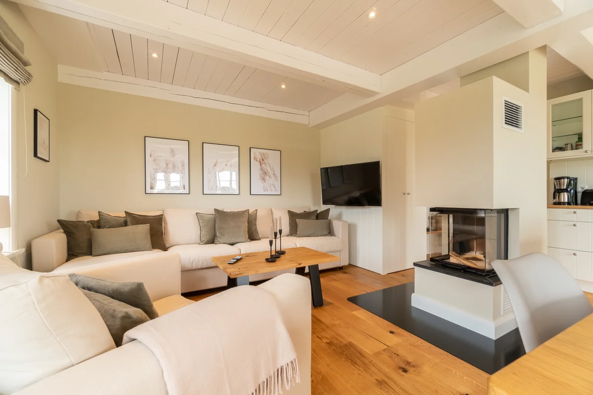 Wohnzimmer mit heller Eckcouch, Couchtisch aus Holz und Kaminofen unter weißer Holzdecke