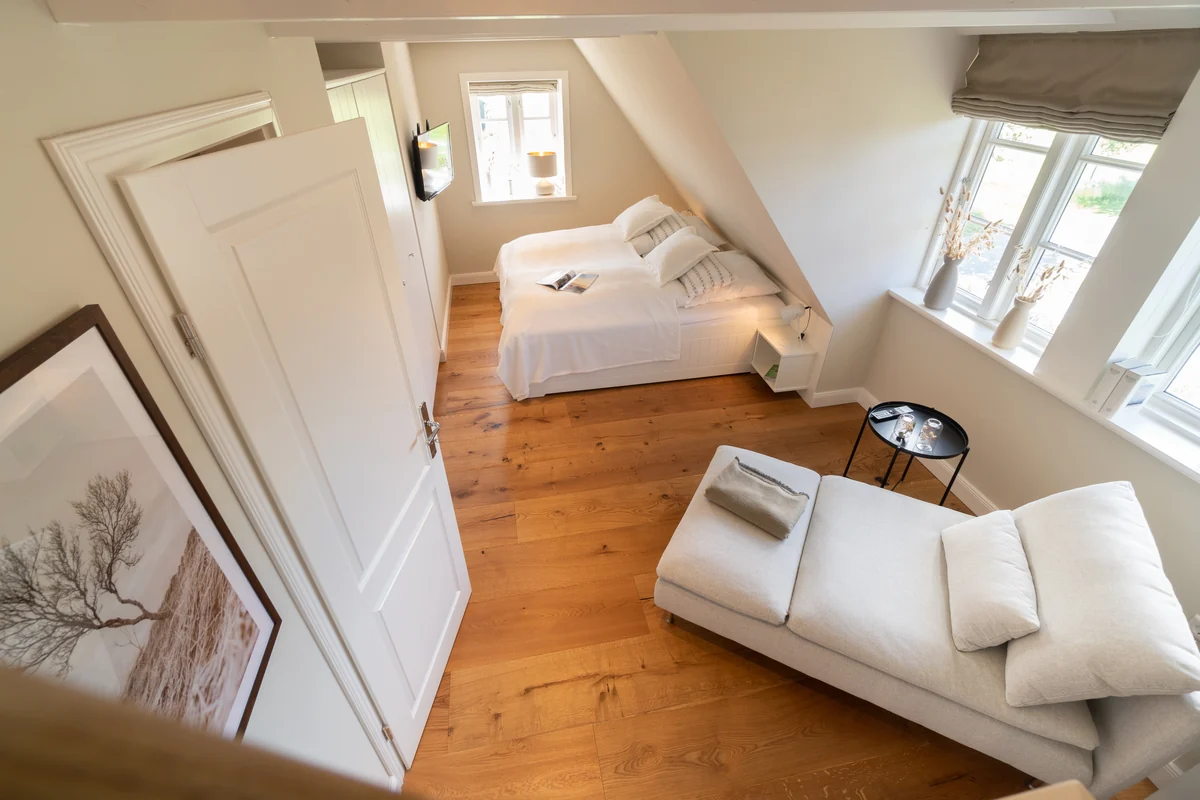 Schlafzimmer unter der Dachschräge mit Doppelbett, Liegesofa und Holzdielen