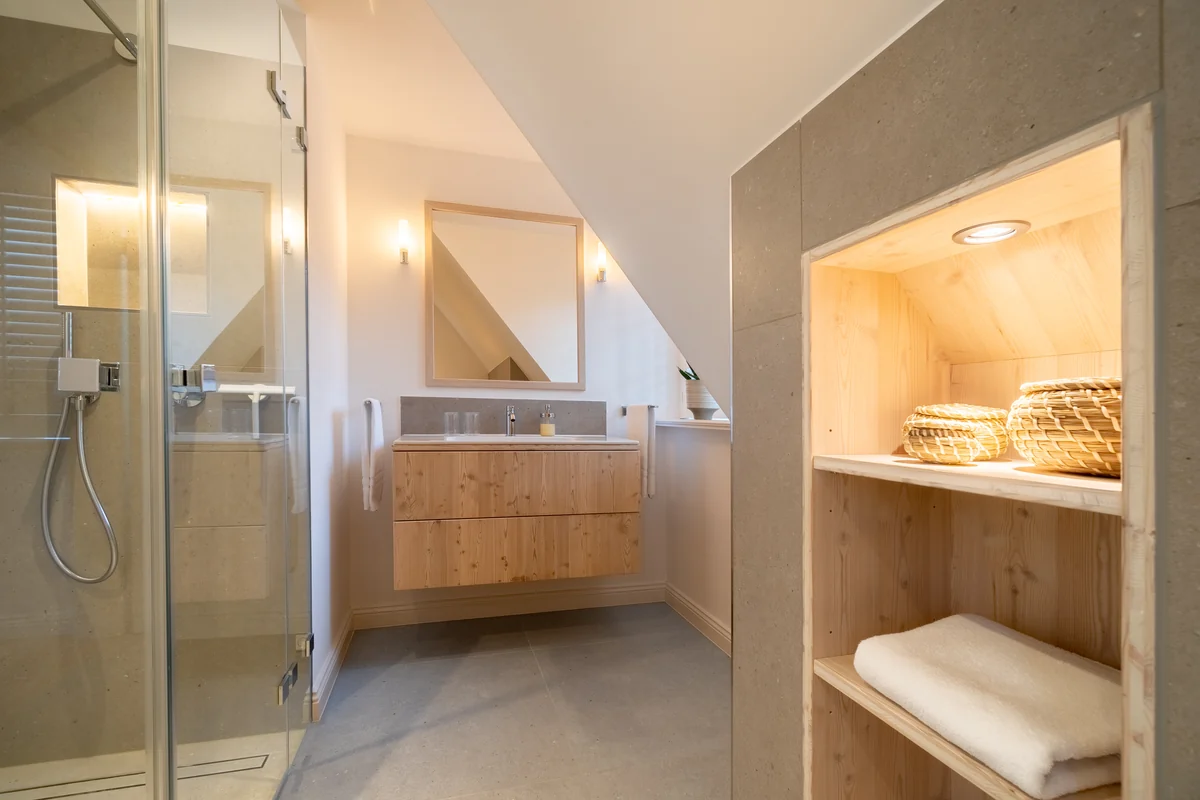 Bad unter der Dachschräge mit Glasdusche, Waschtisch aus Holz und beleuchtetem Wandregal
