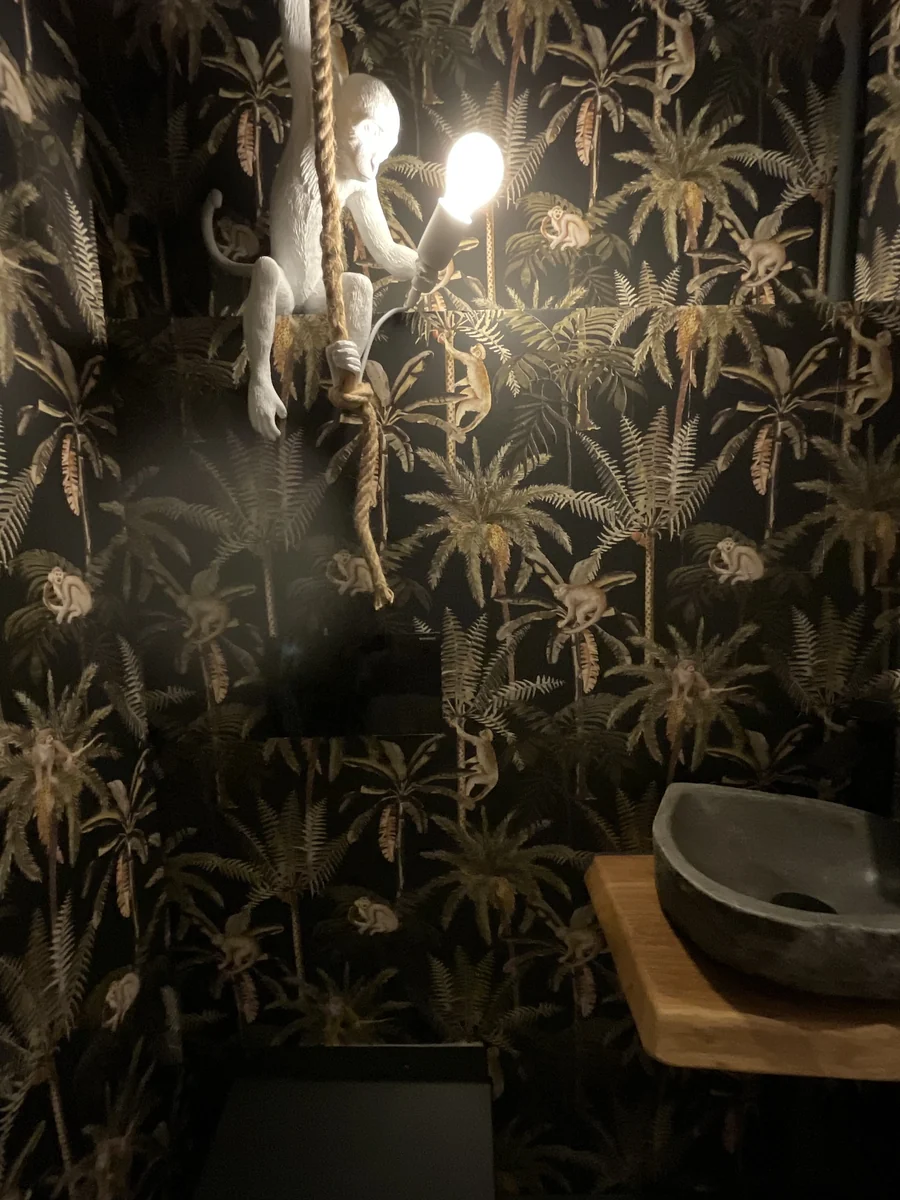 Badezimmer mit dunkler Palmentapete, Steinwaschbecken und Affenleuchte