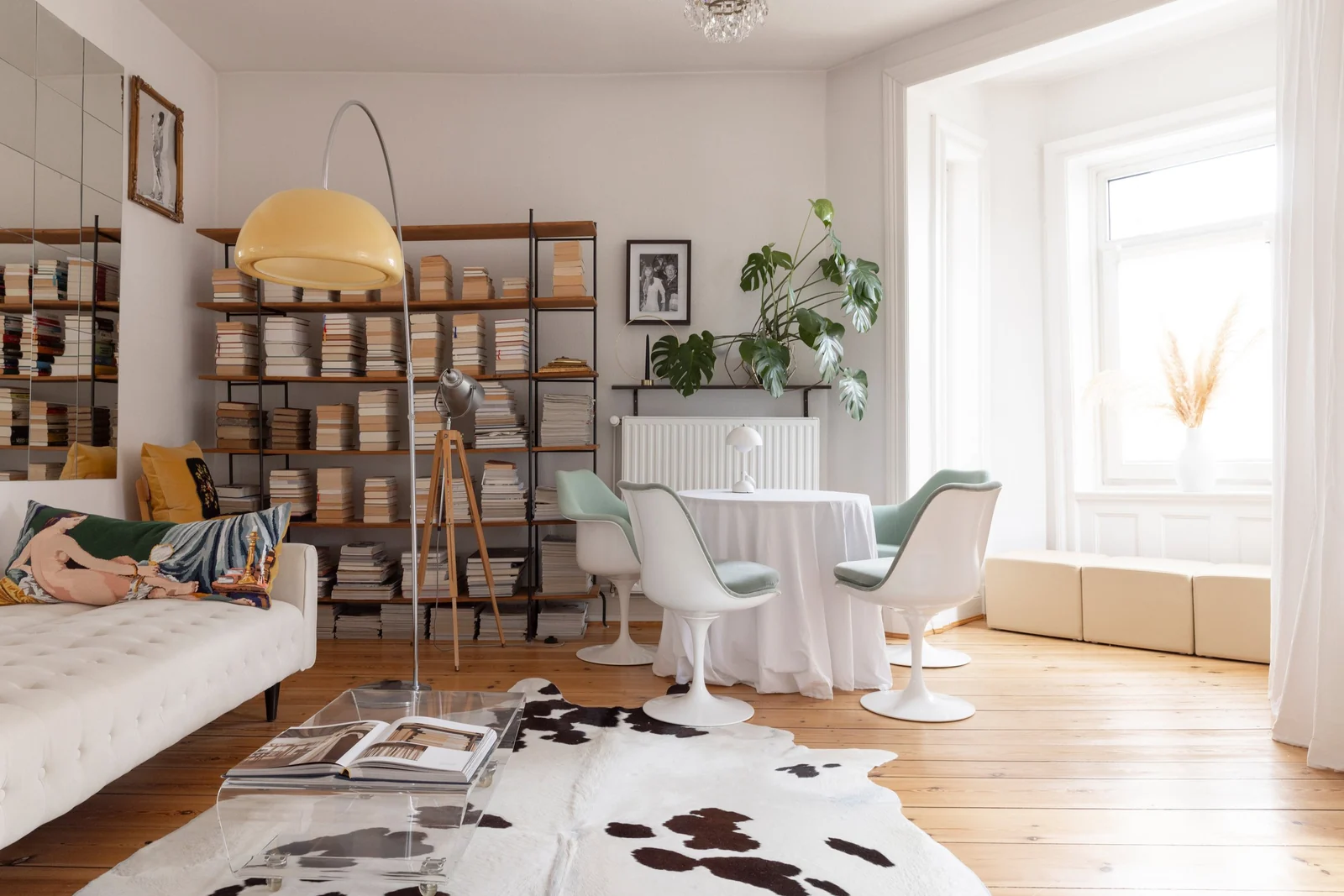 Heller Altbau-Wohnraum mit Bücherregalen, gelber Bogenleuchte, weißen Sesseln und Fellteppich