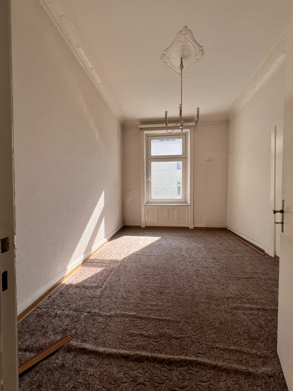 Leerer Altbauraum mit welligem Teppich vor dem Umbau