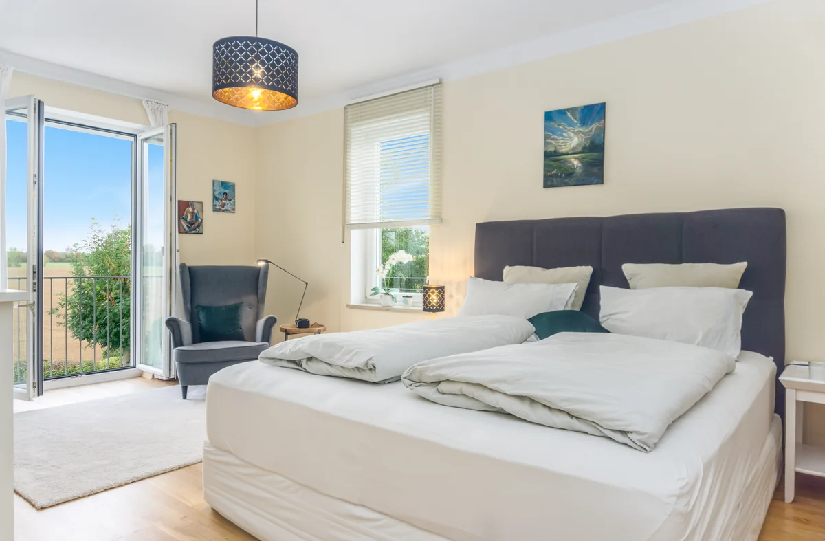 Schlafzimmer mit Doppelbett, Sessel und offener Balkontür