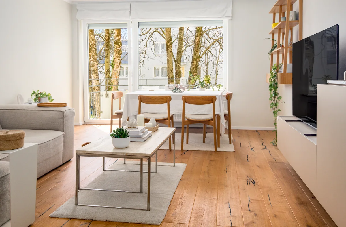 Wohnzimmer mit Holzboden, Sofa, Couchtisch und Essplatz am Fenster