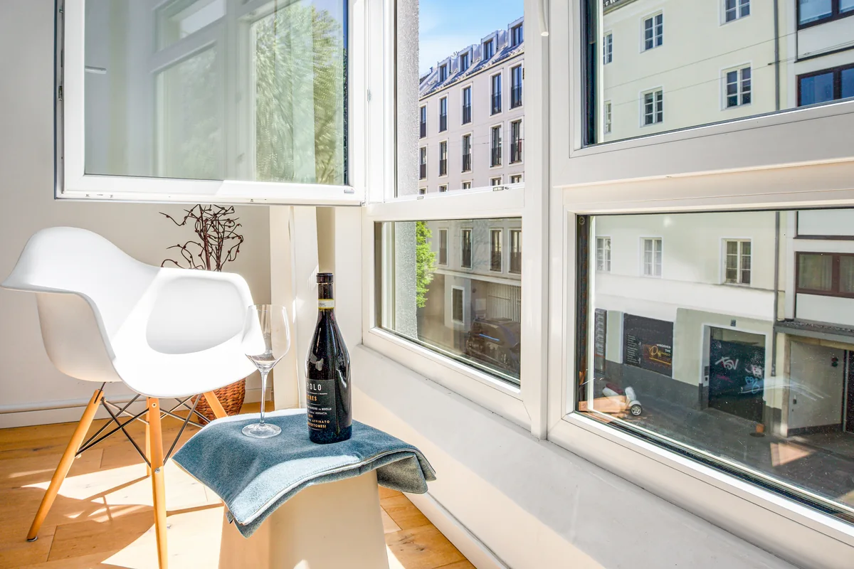 Fensterplatz mit weißem Schalenstuhl, Weinflasche und Blick auf die Stadt
