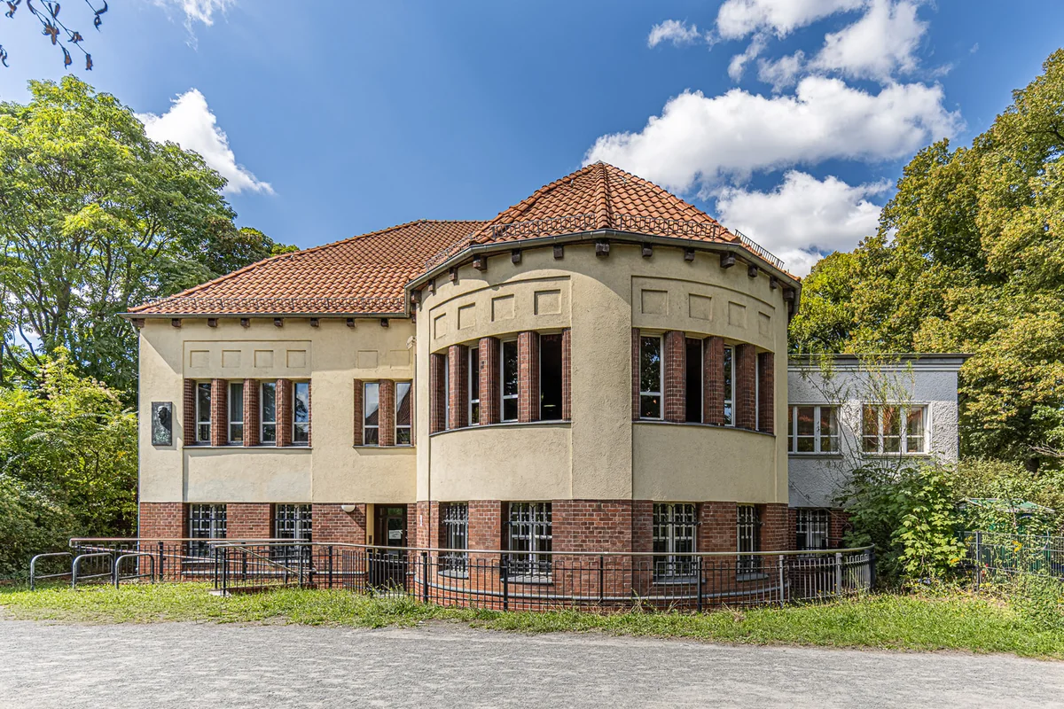 Historisches Haus mit rotem Ziegeldach und Rundbau im Grünen