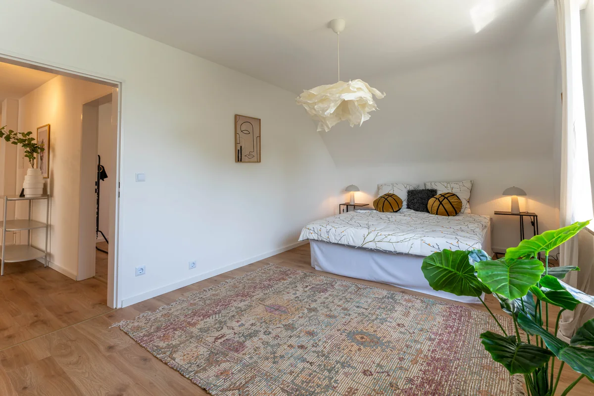 Schlafzimmer mit Doppelbett, Teppich und großer Grünpflanze