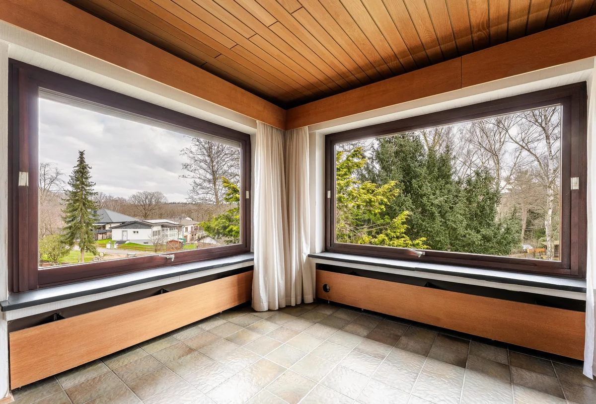 Zimmer mit Holzdecke und zwei großen Panoramafenstern ins Grüne