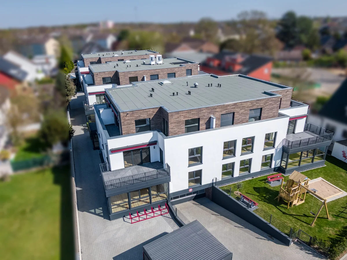 Luftaufnahme eines neuen Mehrfamilienhauses mit Garten und Spielplatz