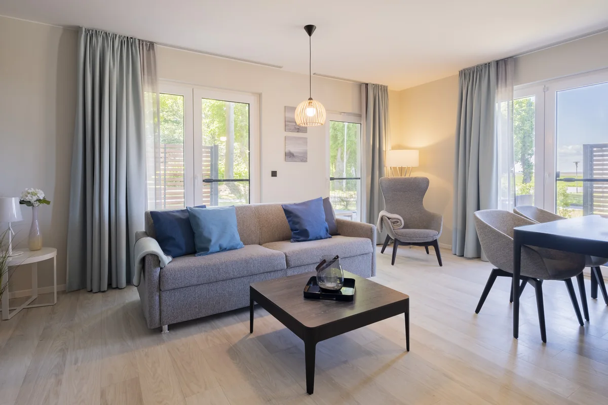 Wohnzimmer mit blauem Sofa, Couchtisch und Essplatz vor bodentiefen Fenstern