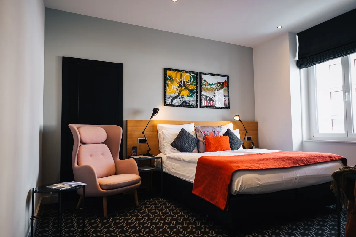 Hotelzimmer mit Doppelbett, rosa Sessel und bunten Bildern