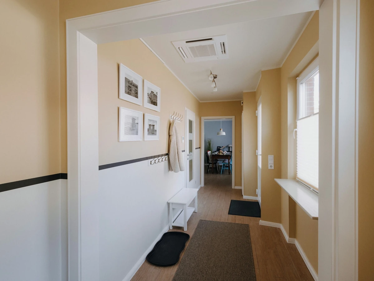 Flur im Haus Juist nachher, mit warmer Wandfarbe, schwarzem Streifen, Bilderrahmen und Läufer
