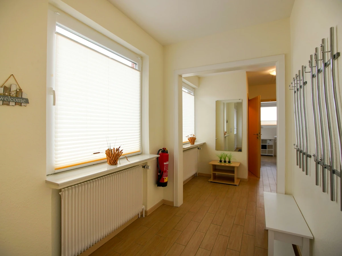 Flur im Haus Juist vorher, mit Heizkörper unter dem Fenster und Garderobe aus Metallstäben