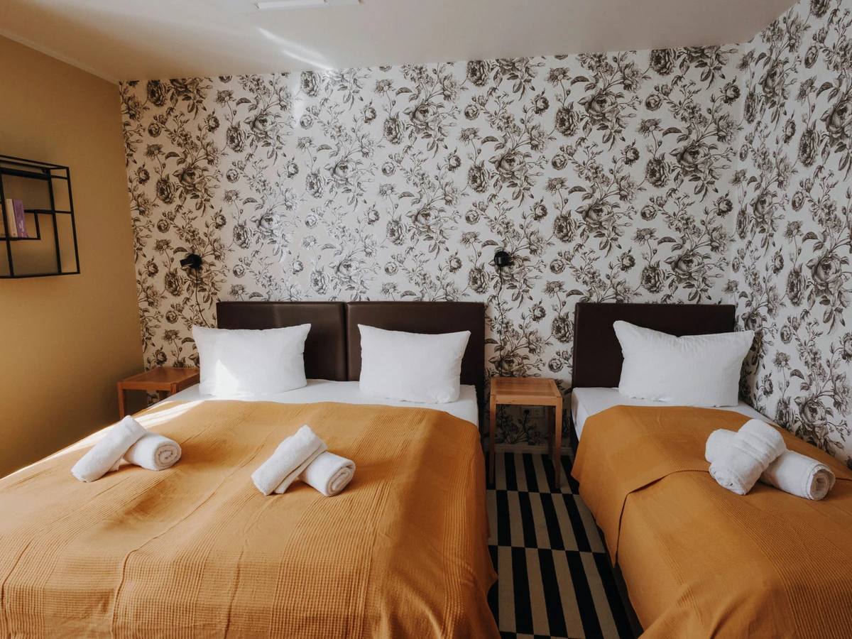 Schlafzimmer im Haus Juist nachher, mit Blumentapete, ockerfarbenen Tagesdecken und gestreiftem Teppich