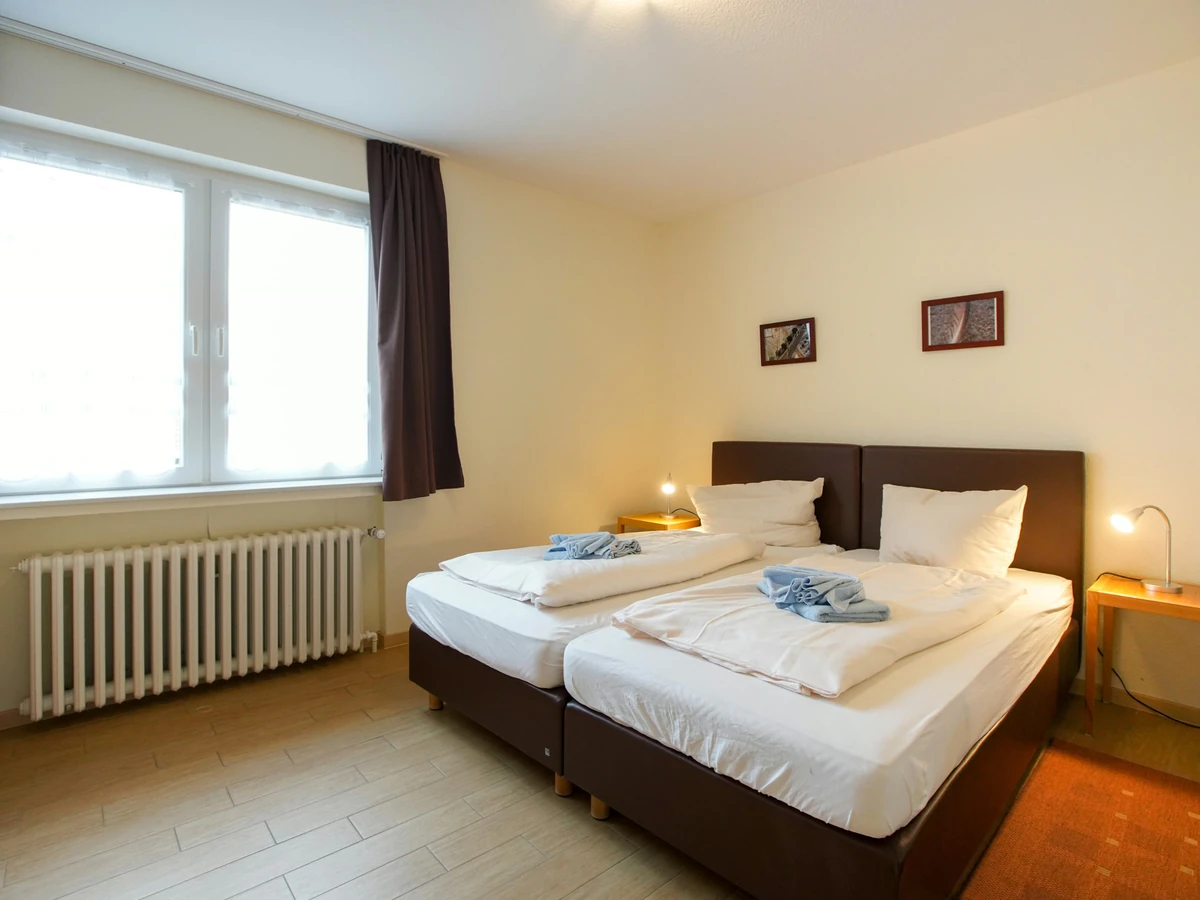 Schlafzimmer im Haus Juist vorher, mit Doppelbett vor heller Wand und dunklen Vorhängen