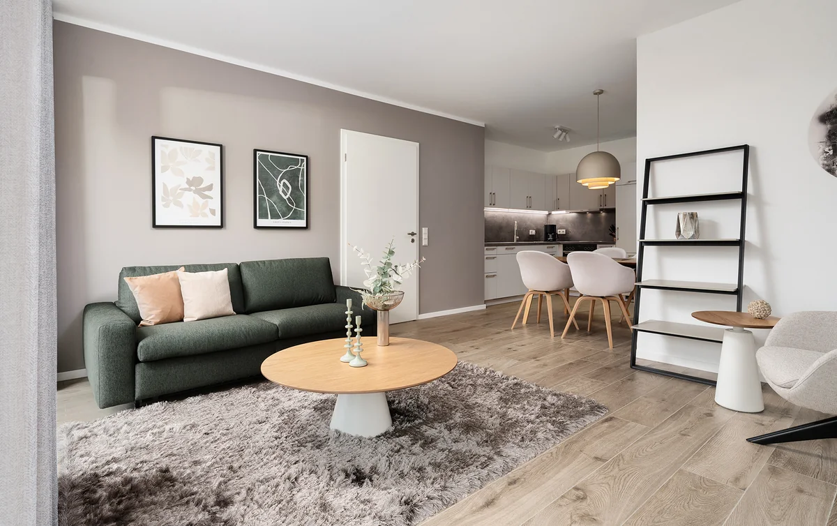 Wohnzimmer einer Ferienwohnung an der Nordsee mit grünem Sofa, Kunstdrucken und rundem Holztisch