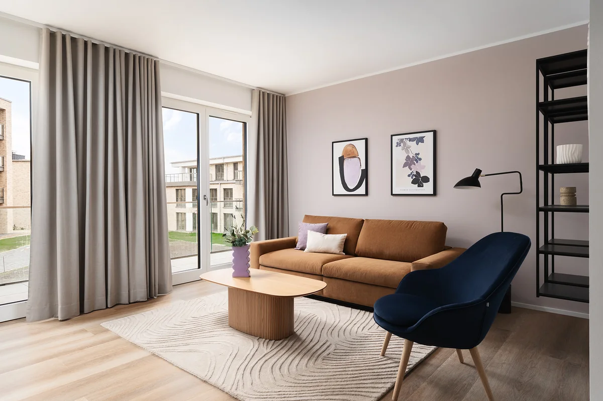 Wohnbereich mit cognacfarbenem Sofa, blauem Sessel und bodenlangen Vorhängen