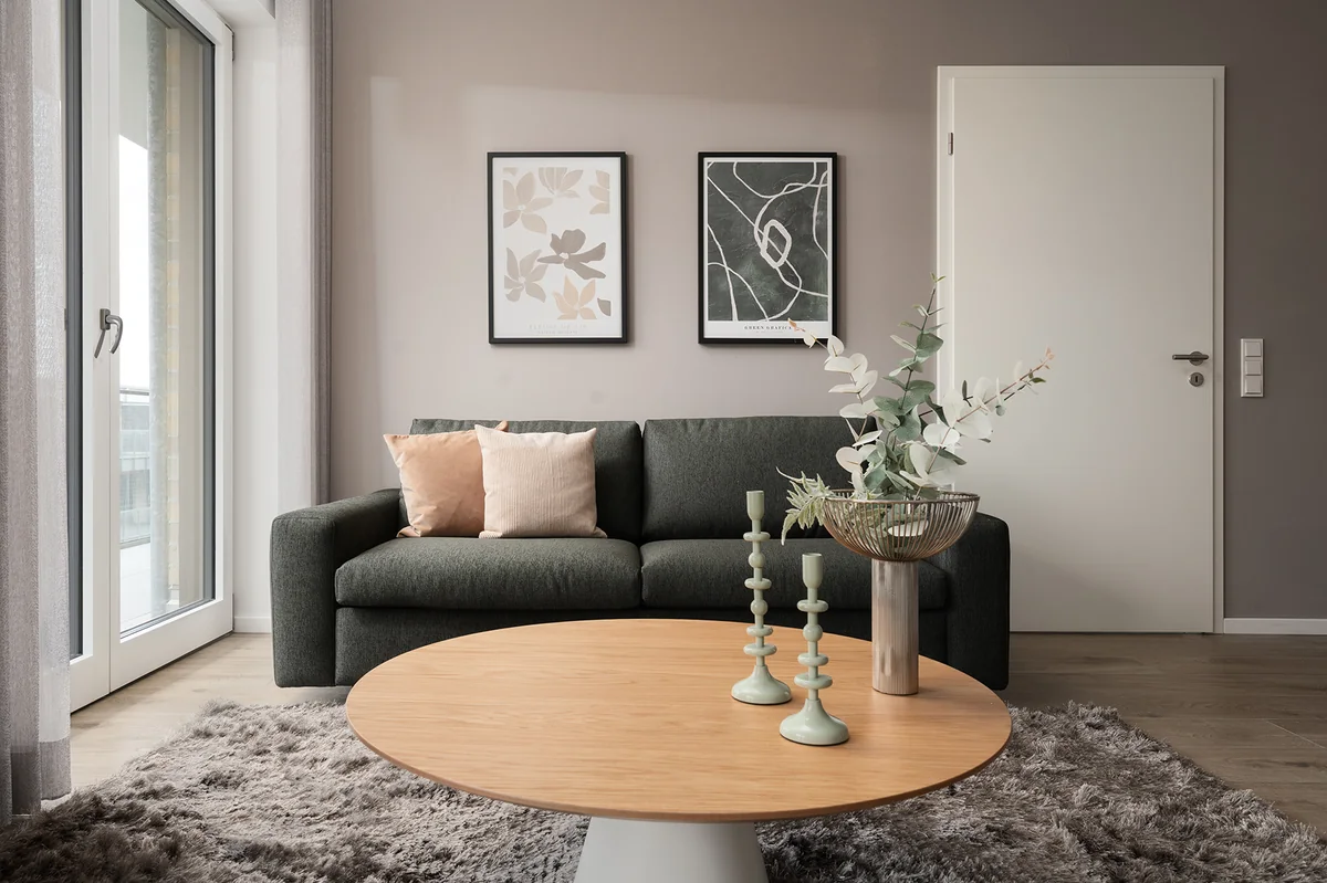 Wohnzimmer mit grünem Sofa, Hochflorteppich und Leiterregal in einer Ferienwohnung