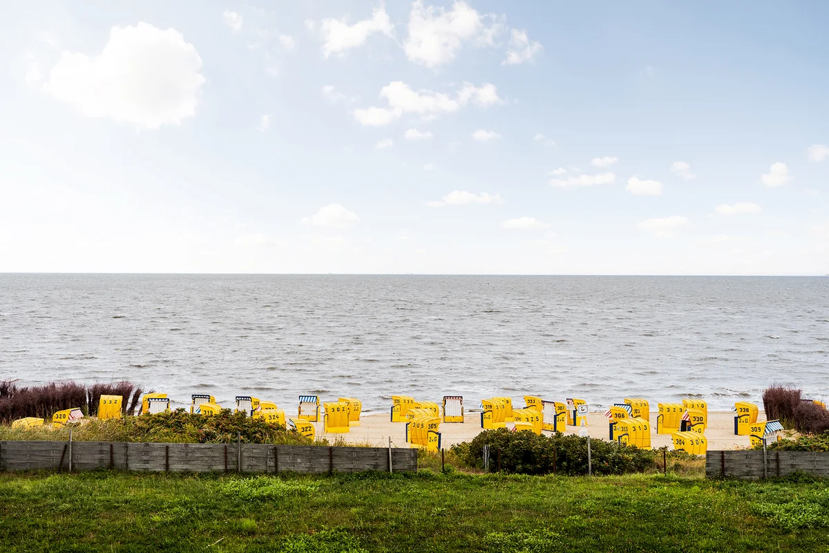 Blick über einen Grünstreifen auf gelbe Strandkörbe und die Nordsee bei Cuxhaven