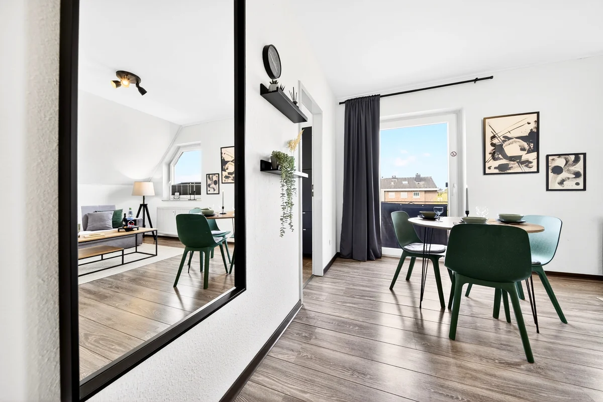 Essplatz mit grünen Stühlen, großem Wandspiegel und Blick zum Balkon