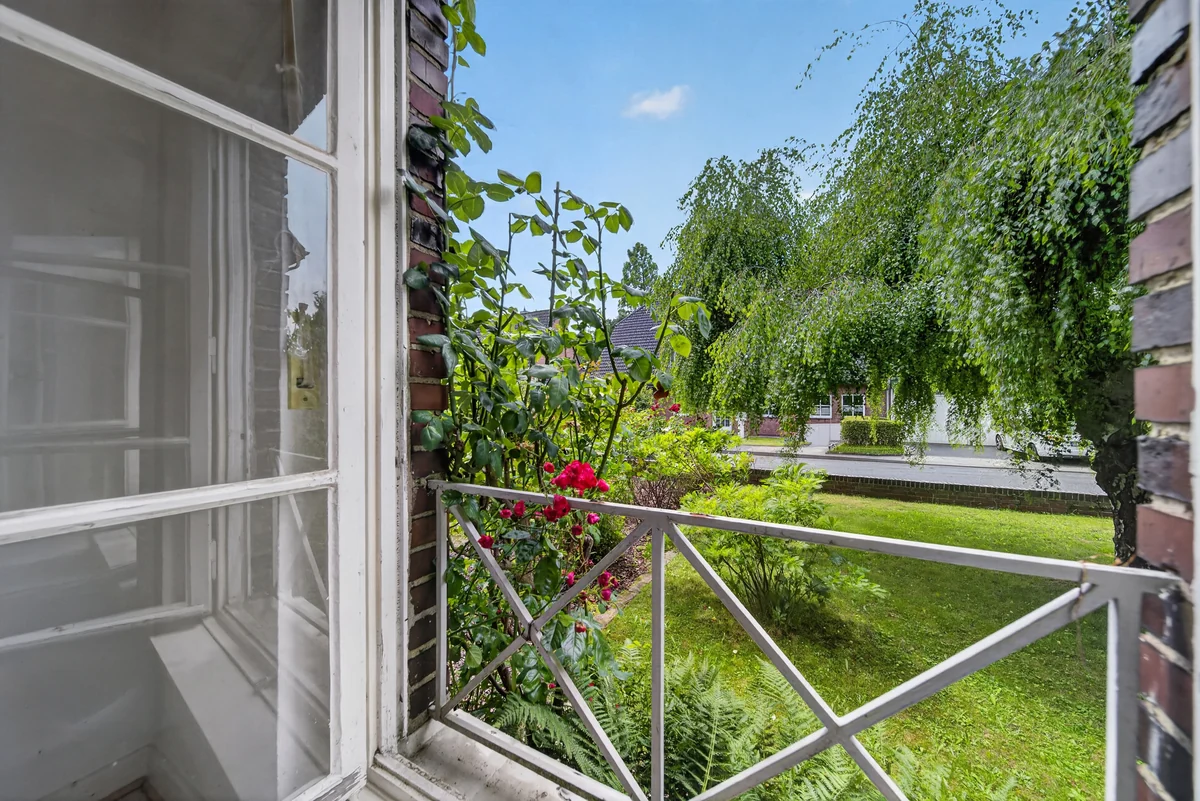 Offene Balkontür mit Blick in einen Garten mit Rosen und Trauerweide