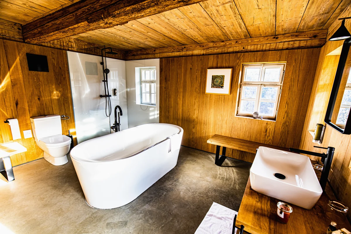 Bad unter einer Holzbalkendecke mit freistehender Badewanne und Aufsatzwaschbecken