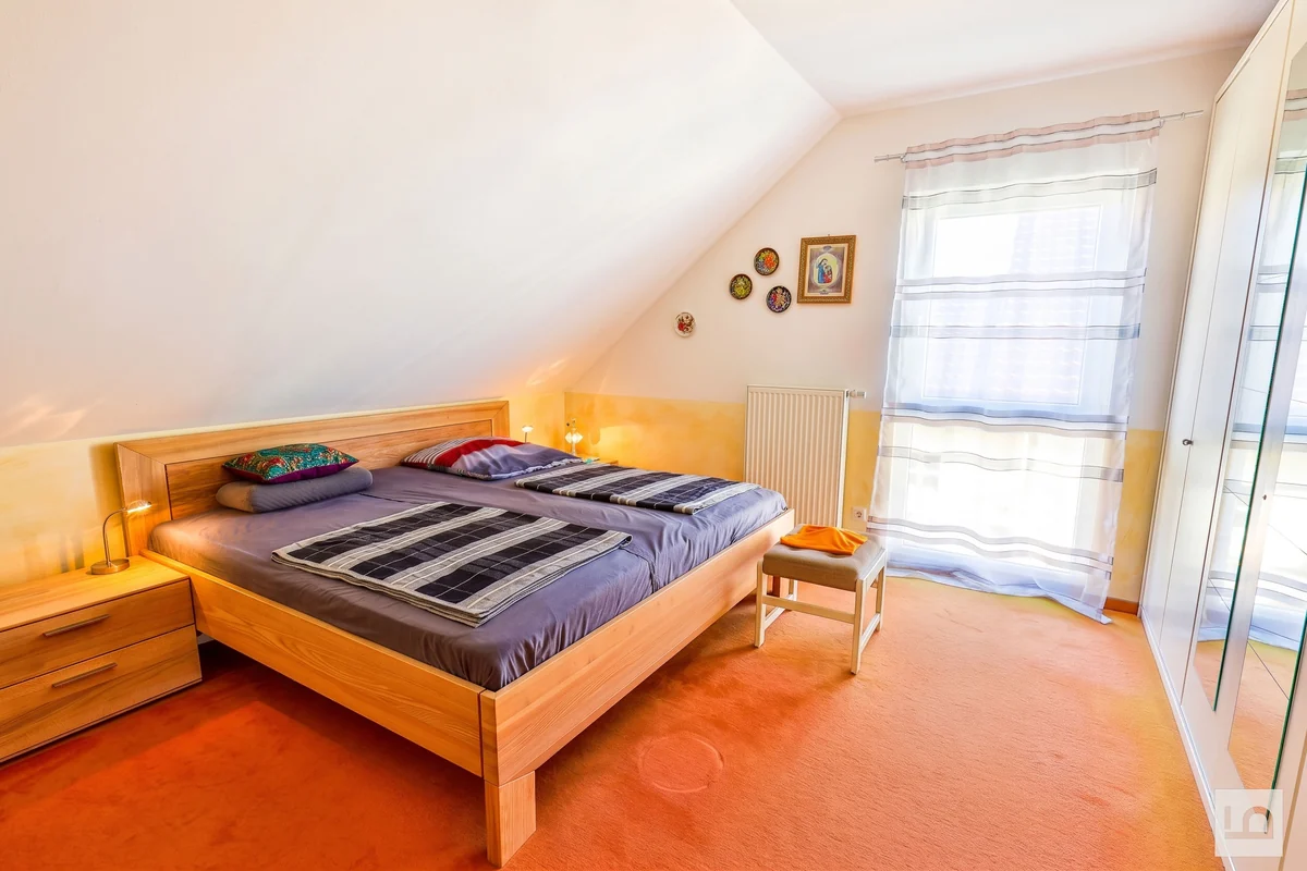 Schlafzimmer unter der Dachschräge mit Holzbett und großem Fenster