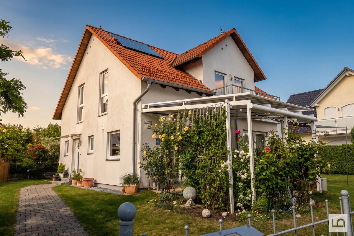 Einfamilienhaus mit rotem Ziegeldach, Pergola und Rosen im Garten