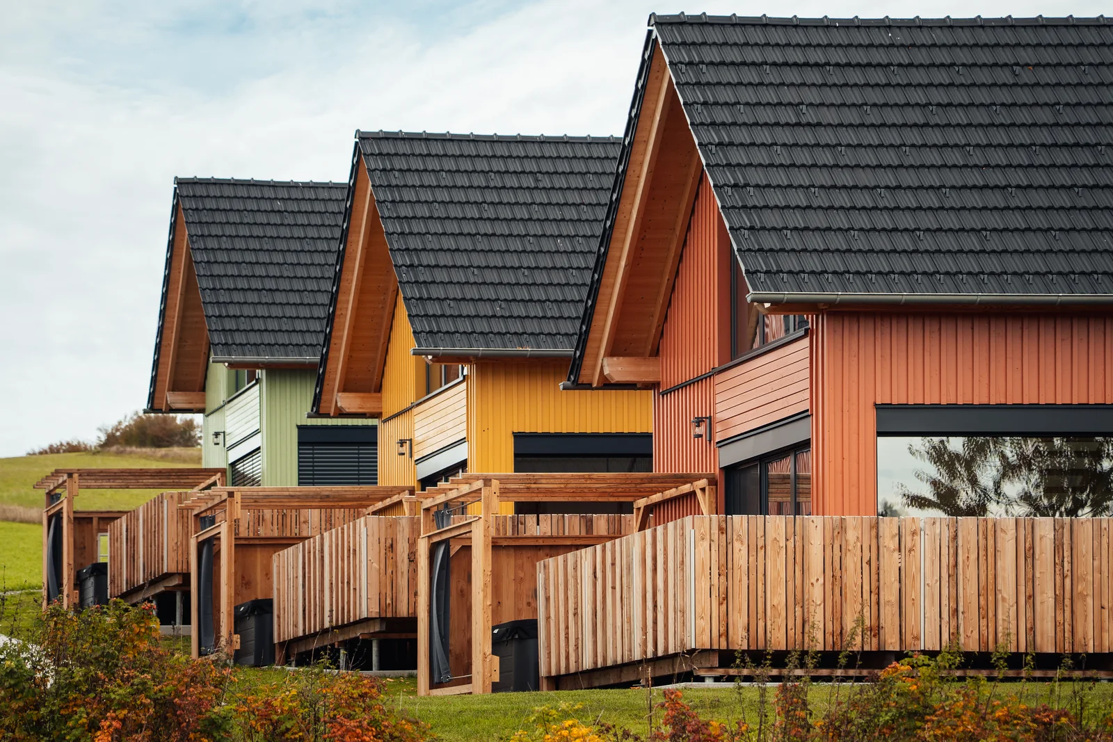 Farbige Holzchalets mit Holzterrassen auf einer Wiese, fotografiert von Stefan Sperl