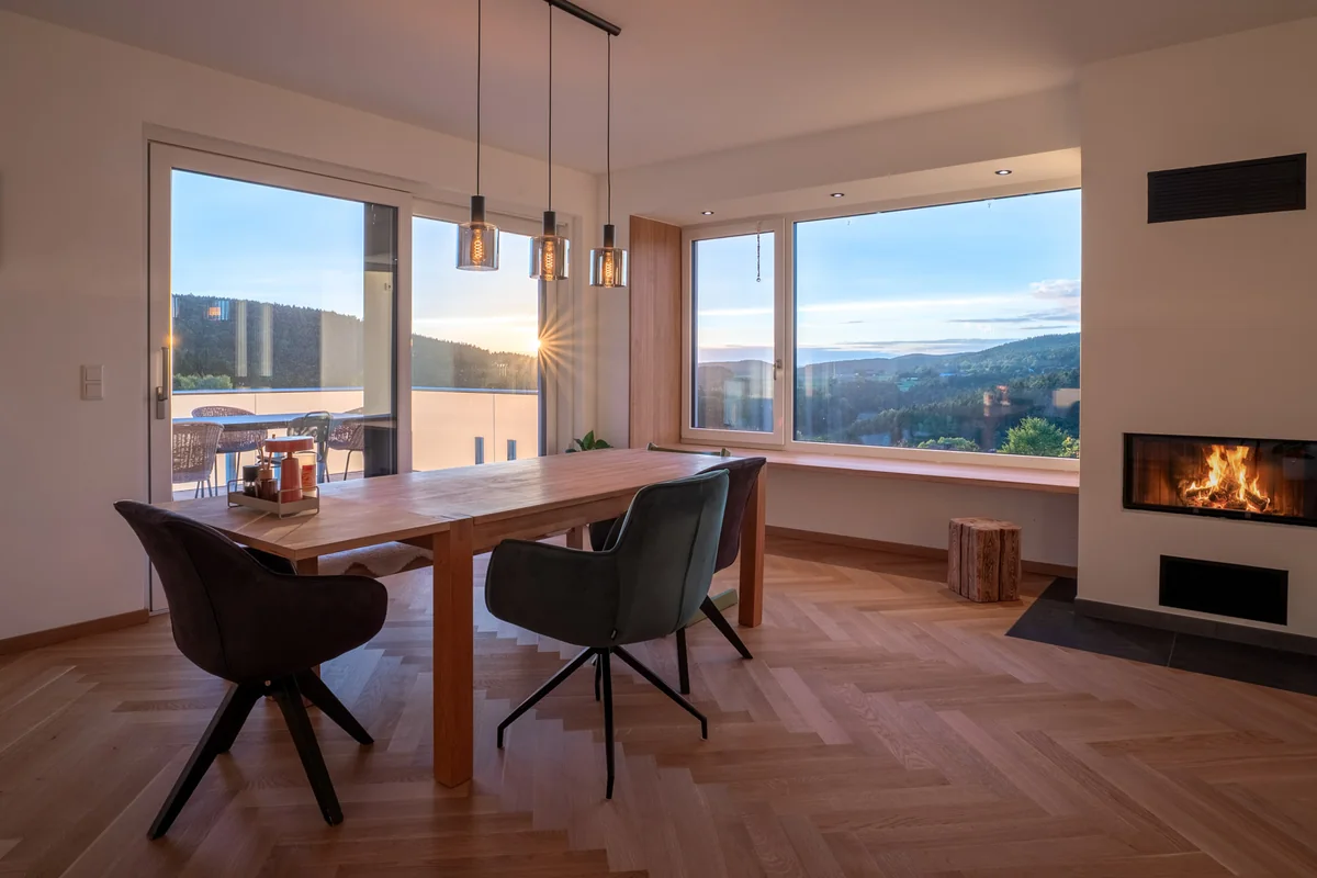 Essbereich mit Holztisch, Kamin und Panoramafenster mit Blick ins Grüne