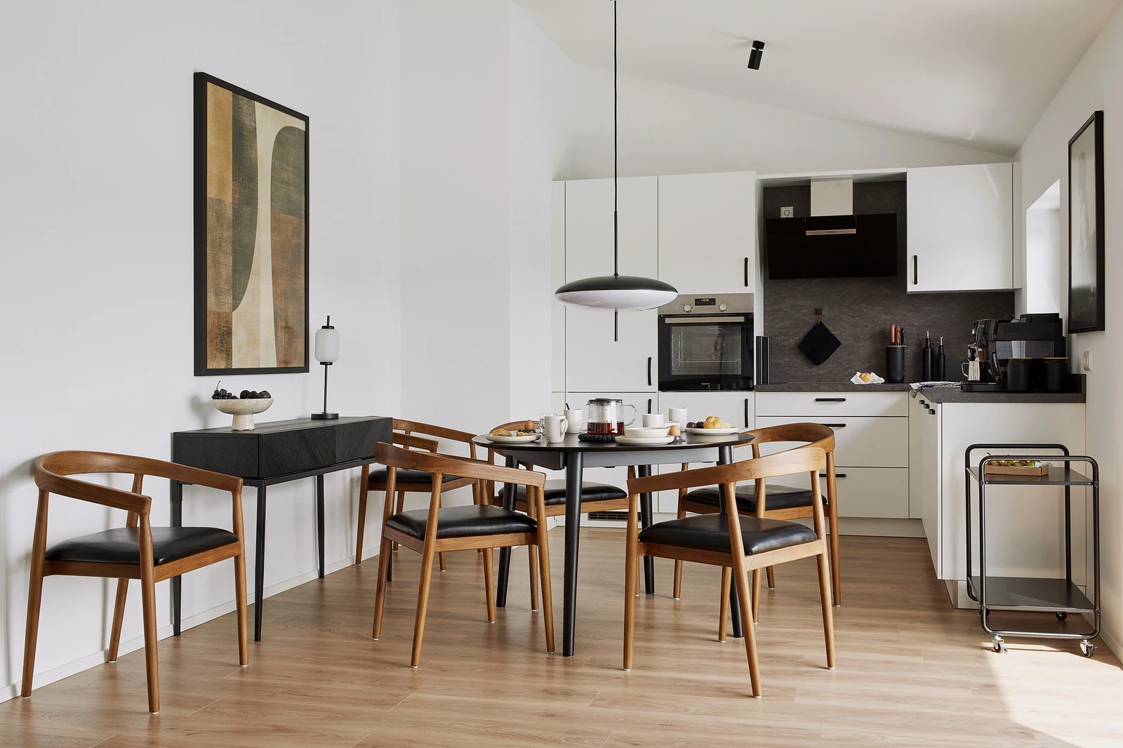 Ess- und Küchenbereich einer Ferienwohnung der Matt Apartments in Offenburg mit Holzstühlen, schwarzem Tisch und abstraktem Bild