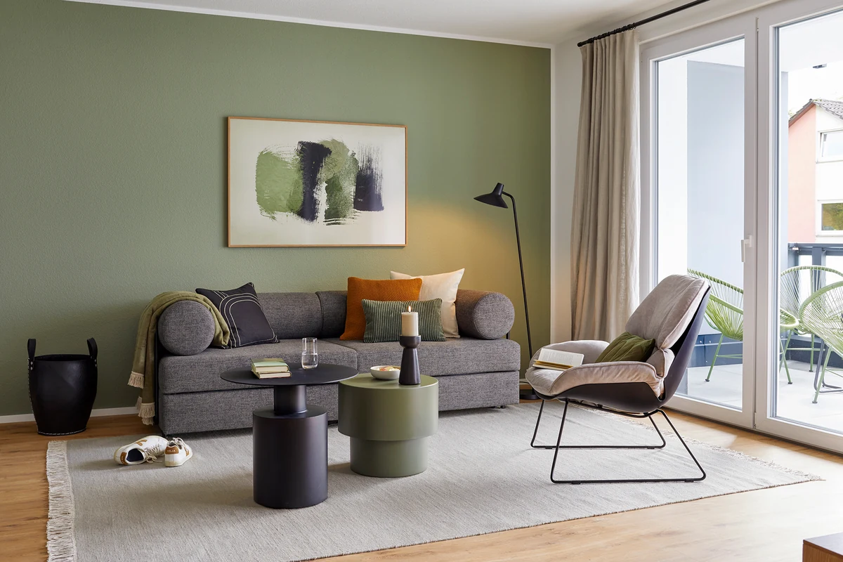 Wohnzimmer mit salbeigrüner Wand, grauem Sofa und Sessel in einer Ferienwohnung der Matt Apartments in Villingen-Schwenningen