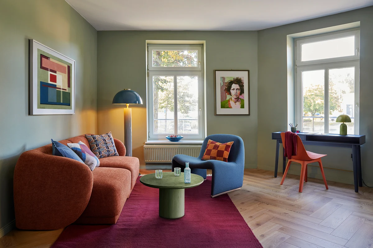Farbenfrohes Wohnzimmer der Ferienwohnung Bach + Leonhardt in Chemnitz mit rostrotem Sofa, blauem Sessel und Kunst an der Wand