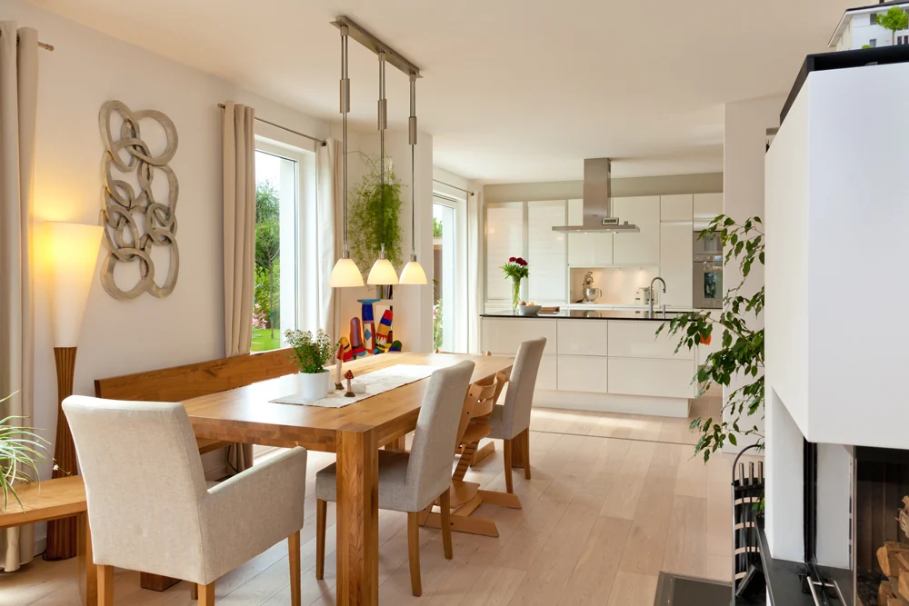 Essbereich mit Holztisch und Polsterstühlen, dahinter eine helle Küche