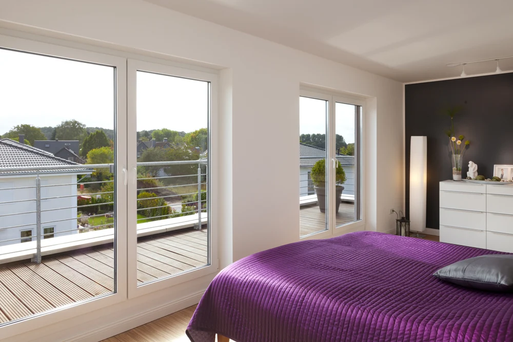 Schlafzimmer mit lila Tagesdecke und Fenstertür zum Balkon