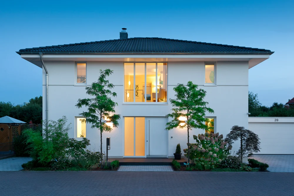 Weißes Einfamilienhaus mit beleuchteten Fenstern zur Blauen Stunde