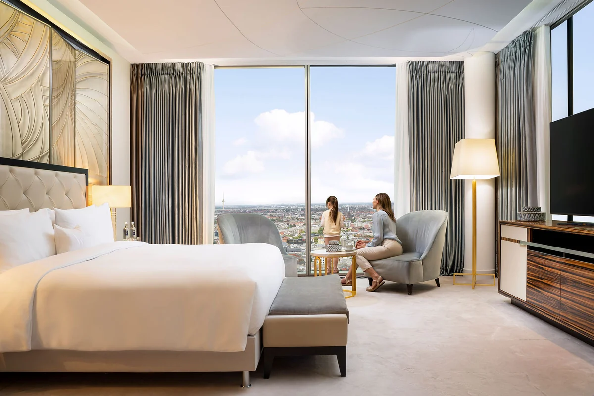 Hotelzimmer mit Doppelbett, Sitzecke und bodentiefen Fenstern über der Stadt
