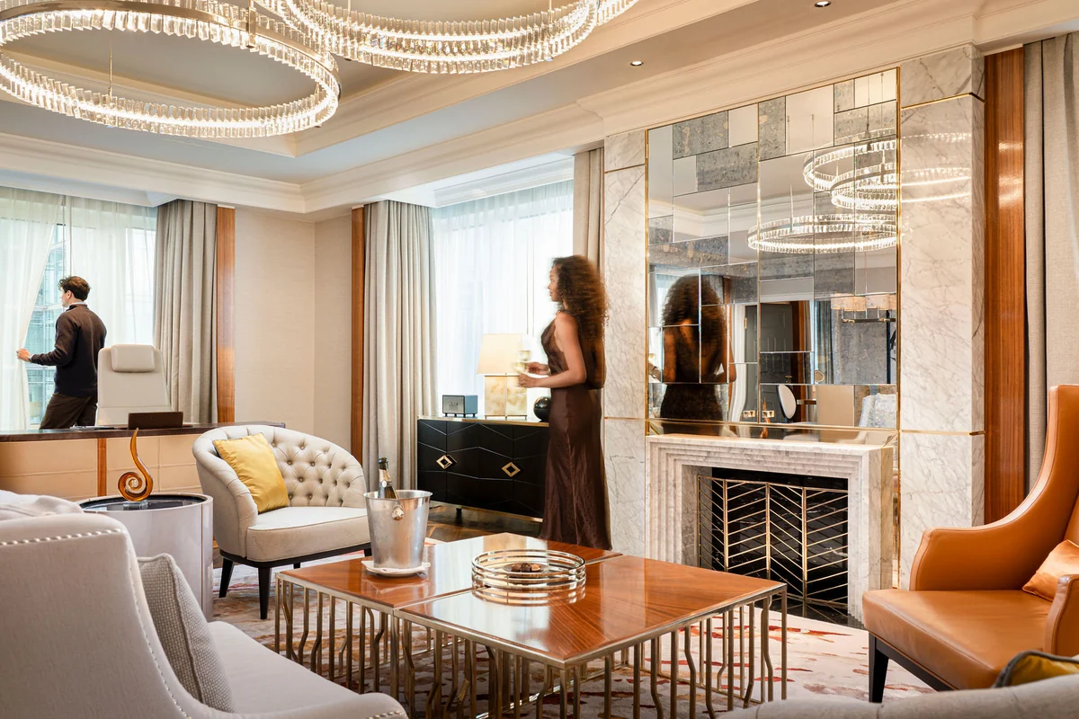 Hotelsuite mit Kamin, Lichtringen an der Decke und Sesseln, dahinter zwei Gäste
