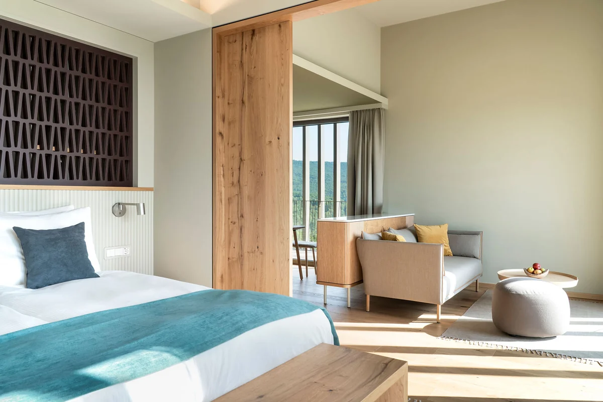 Helles Zimmer mit Bett, Holzwand und Sitzecke am Fenster